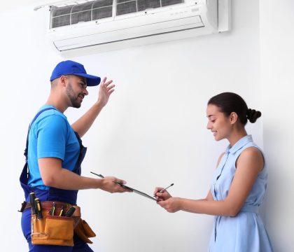 Professional technician speaking with woman about air conditioner indoors Professional technician speaking with woman about air conditioner indoors
